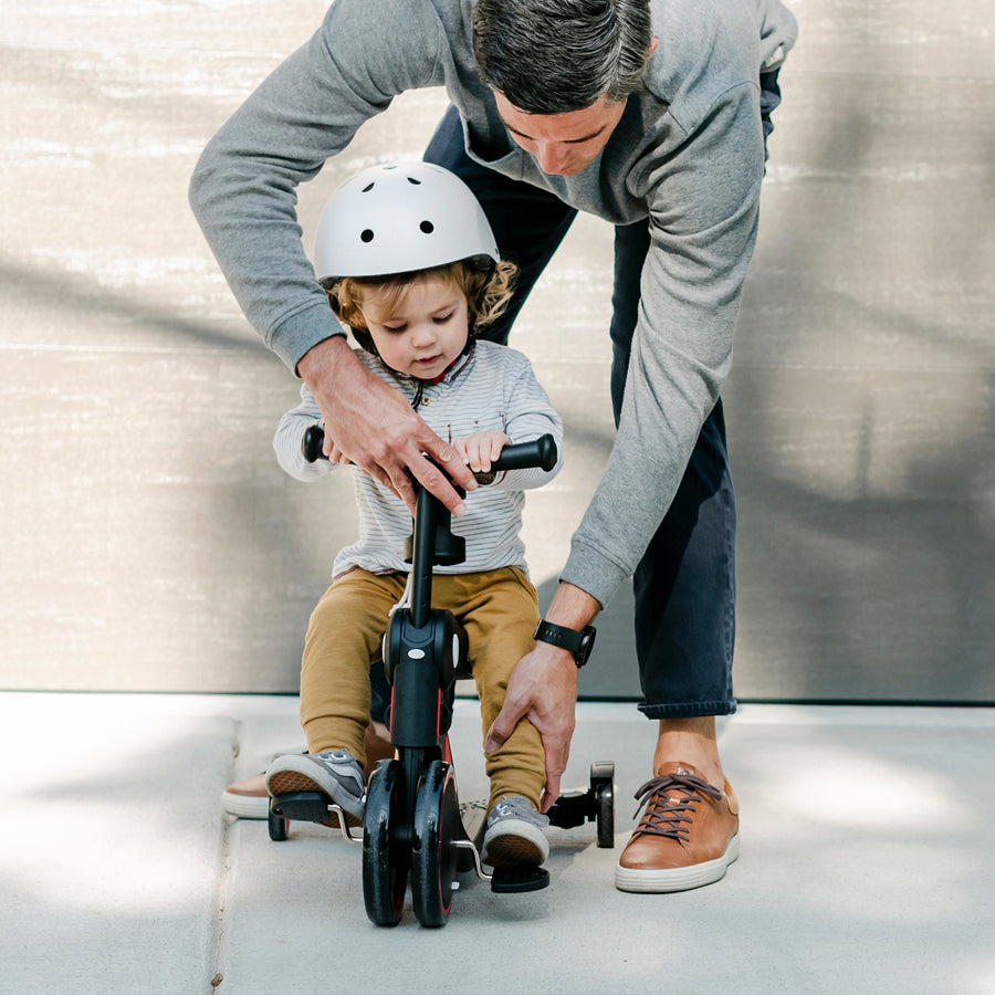 dad helps child pedal on the tricycle mode
