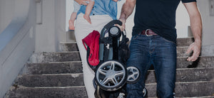 Coast stroller. small fold stroller. Lightweight stroller. Compact Fold. Easy to carry stroller. Image: father carries the lightweight folded coast stroller down a flight of stairs