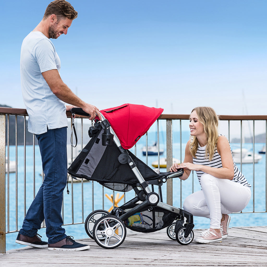 family sits on a boat dock with the coast stroller in red