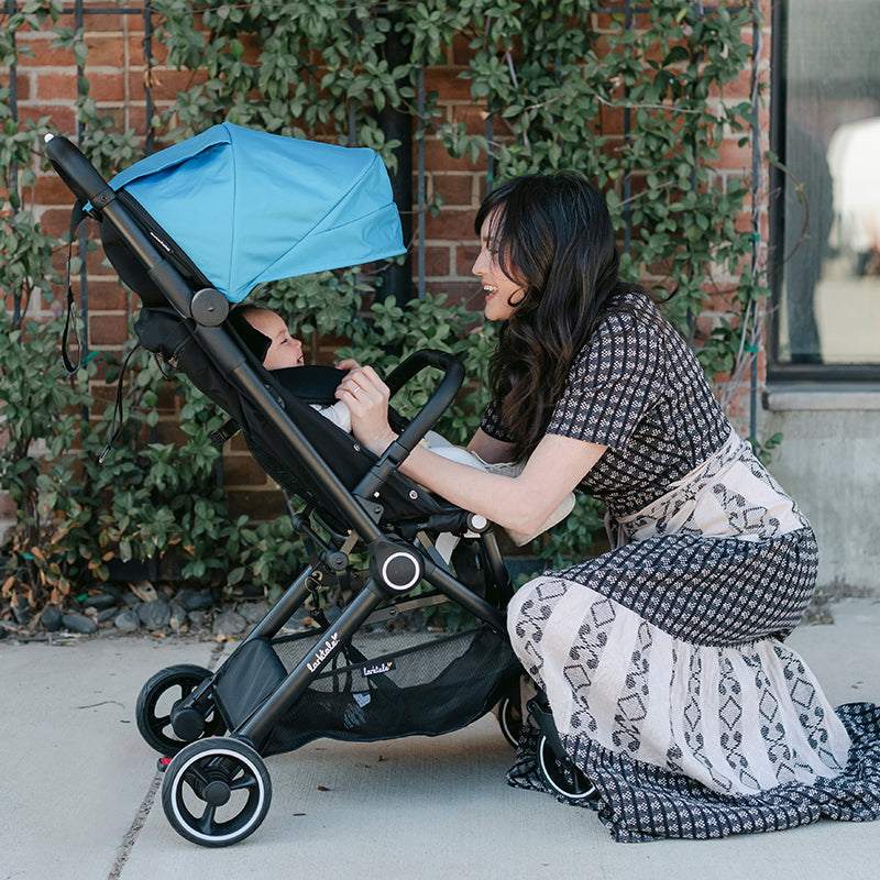mom kneels by baby in autofold stroller in freshwater blue