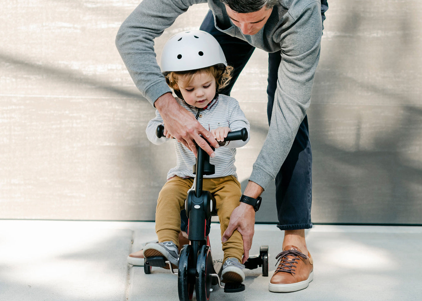 toddler sitting on the scoobi 5-in-one scooter with help of a parent