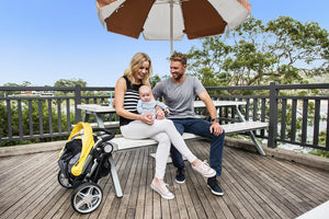 family sits at a picnic table with the coast stroller folded nearby